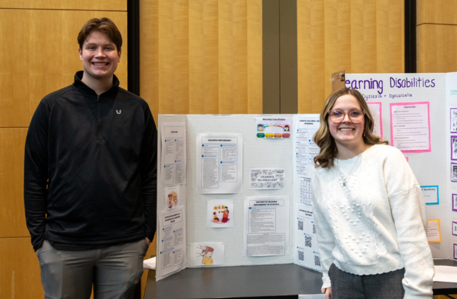 a man and woman standing next to a poster board