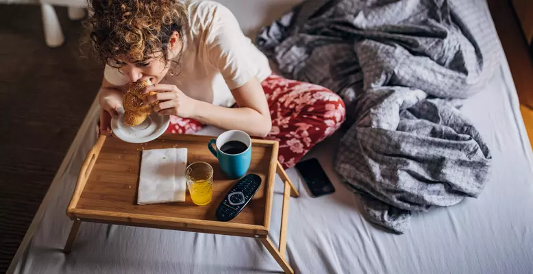a woman sitting on a bed eating a sandwich a woman sitting on a bed eating a sandwich