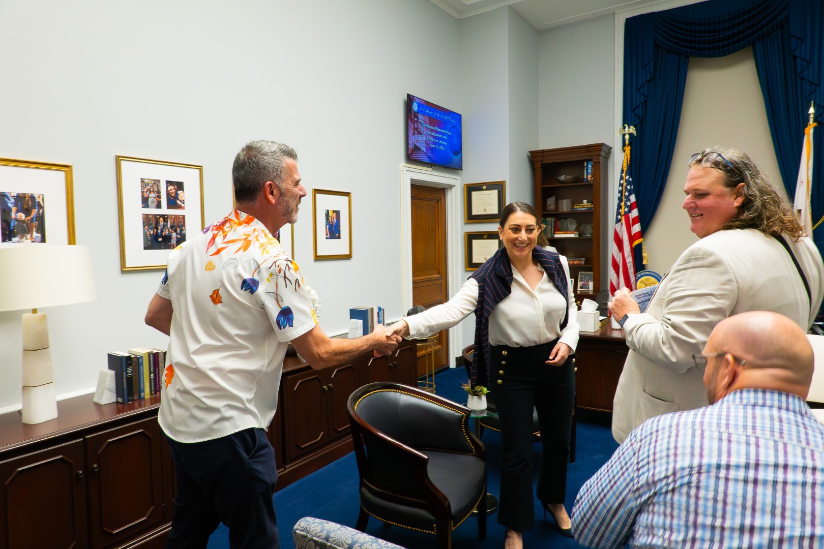 Symposium attendee shaking hands with a woman in a room with a flag