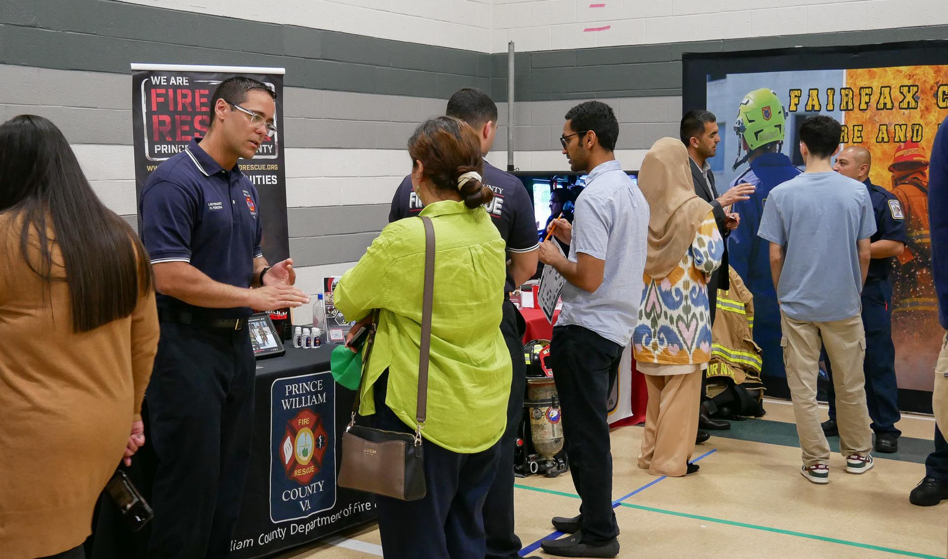 Diverse adults mingle and talk to recruiters at a career fair that includes representatives from Prince William and Fairfax fire and rescue services