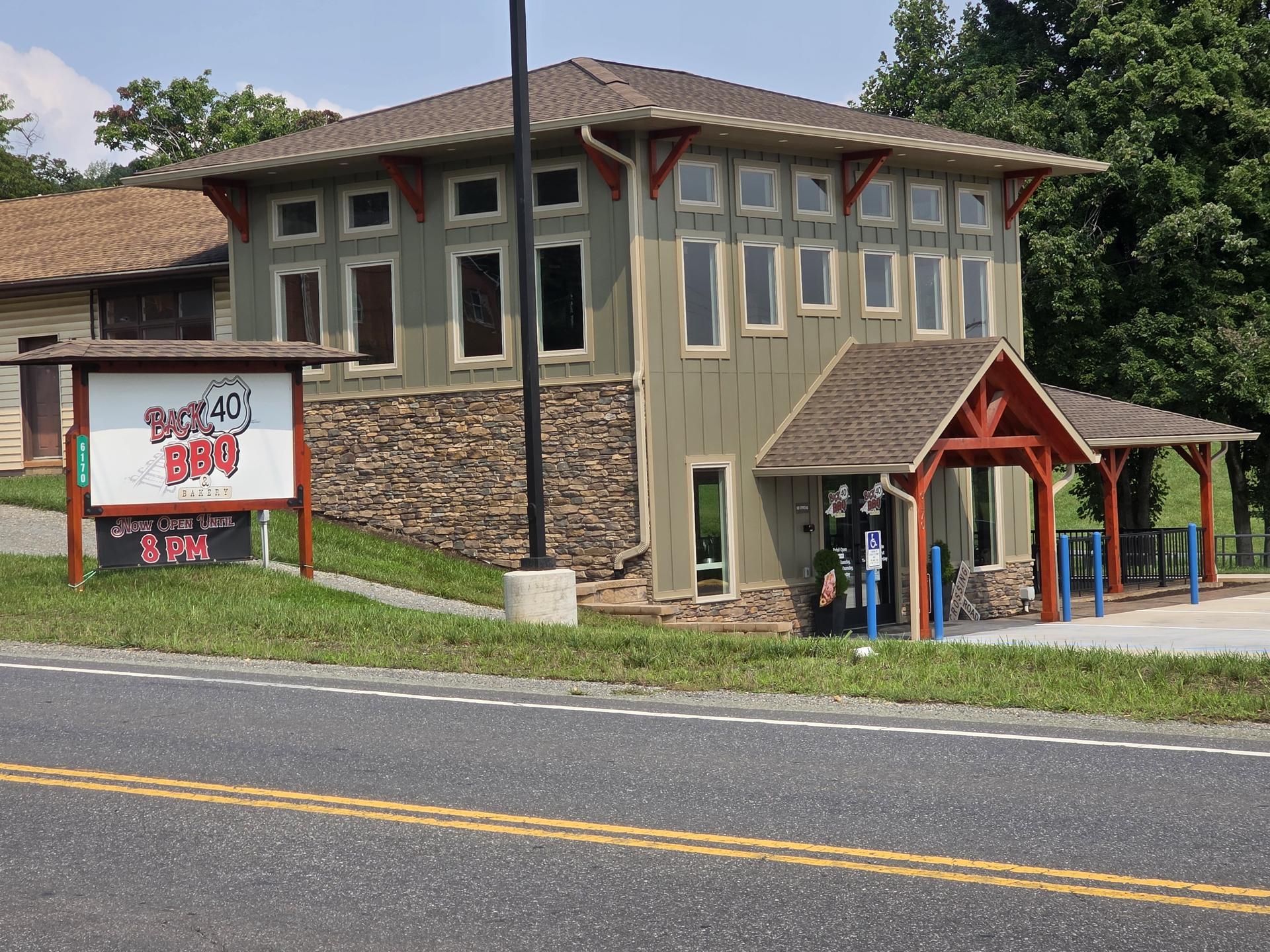 Photograph of a roadside building with tan siding, a welcoming barn-style entry, and a sign reading Back 40 BBQ