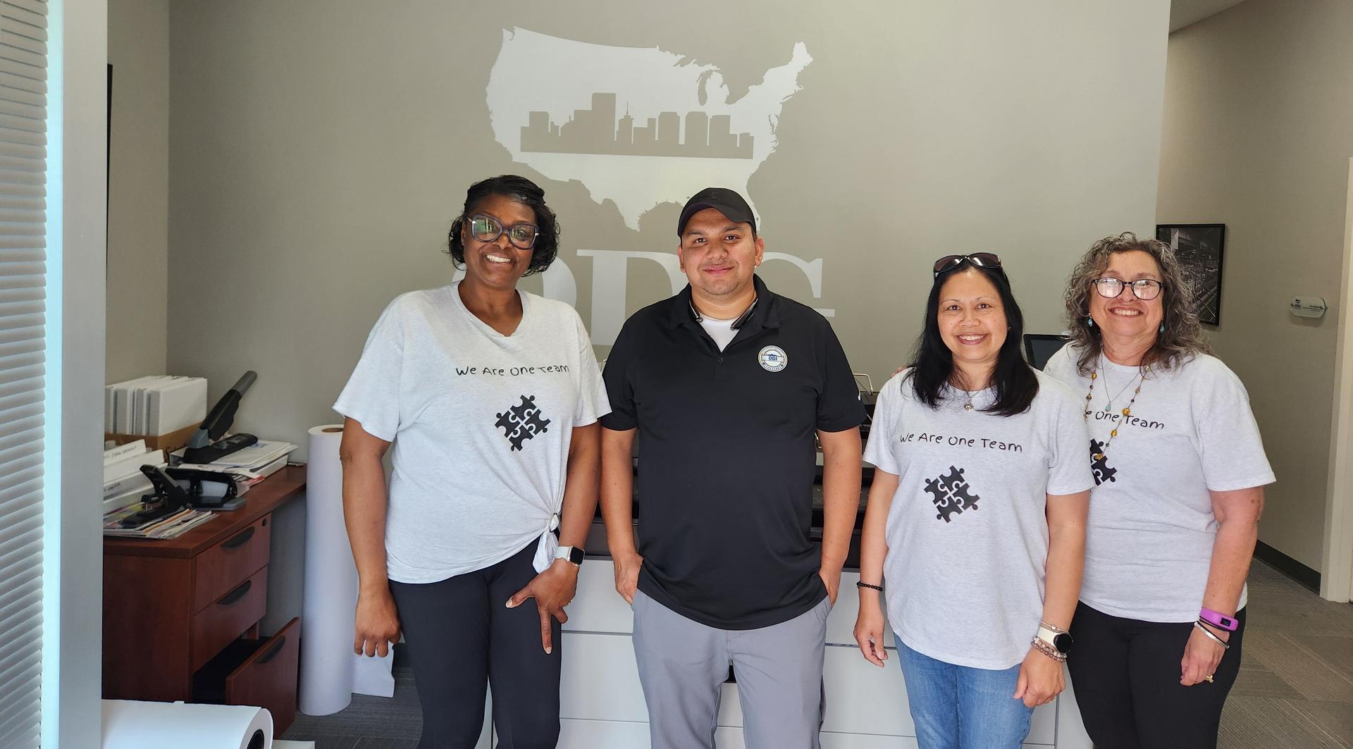 group photo of smiling adults in an office wearing T-shirts that read We Are One Team
