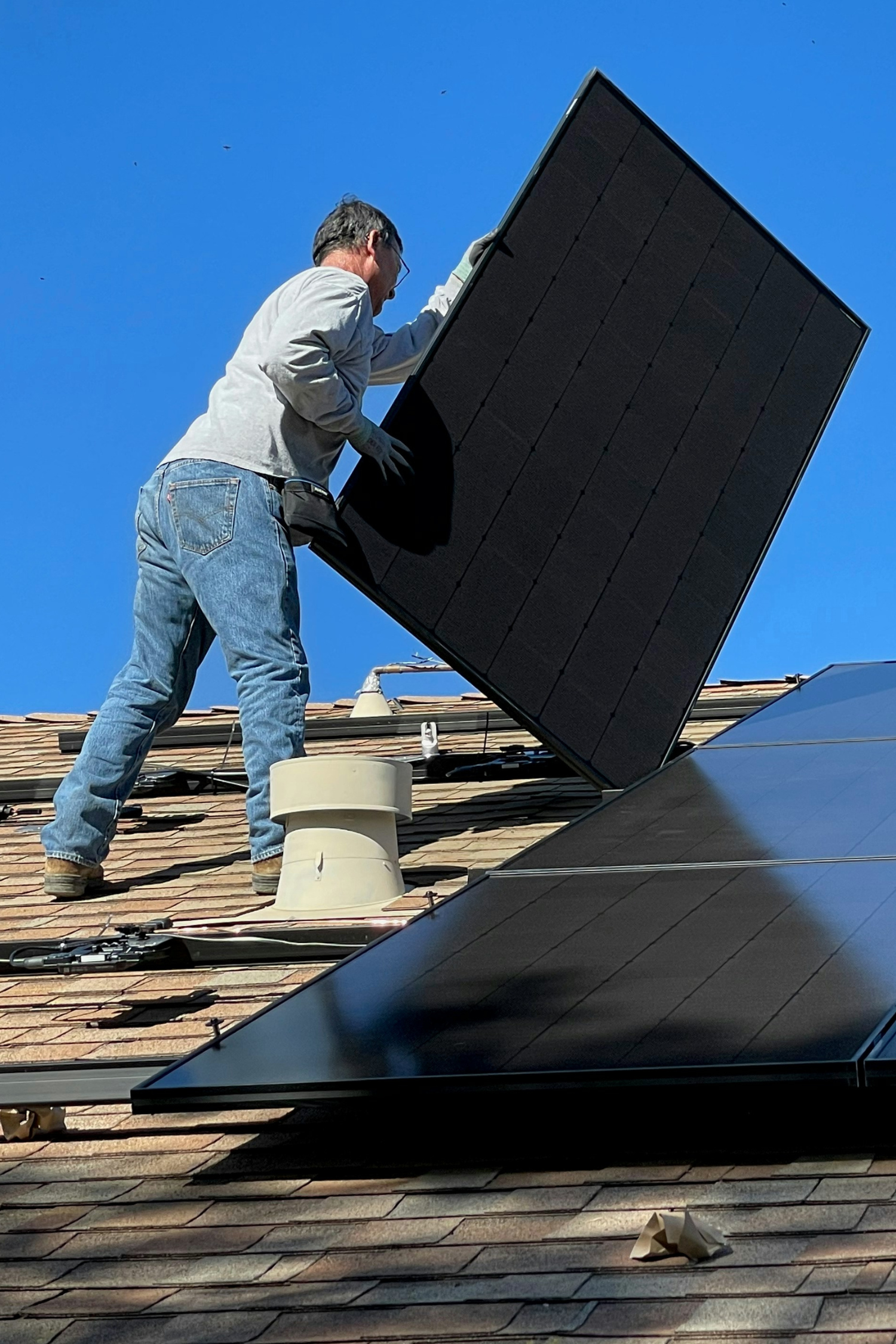 stock photo shows a worker on a roof, installing a solar panel
