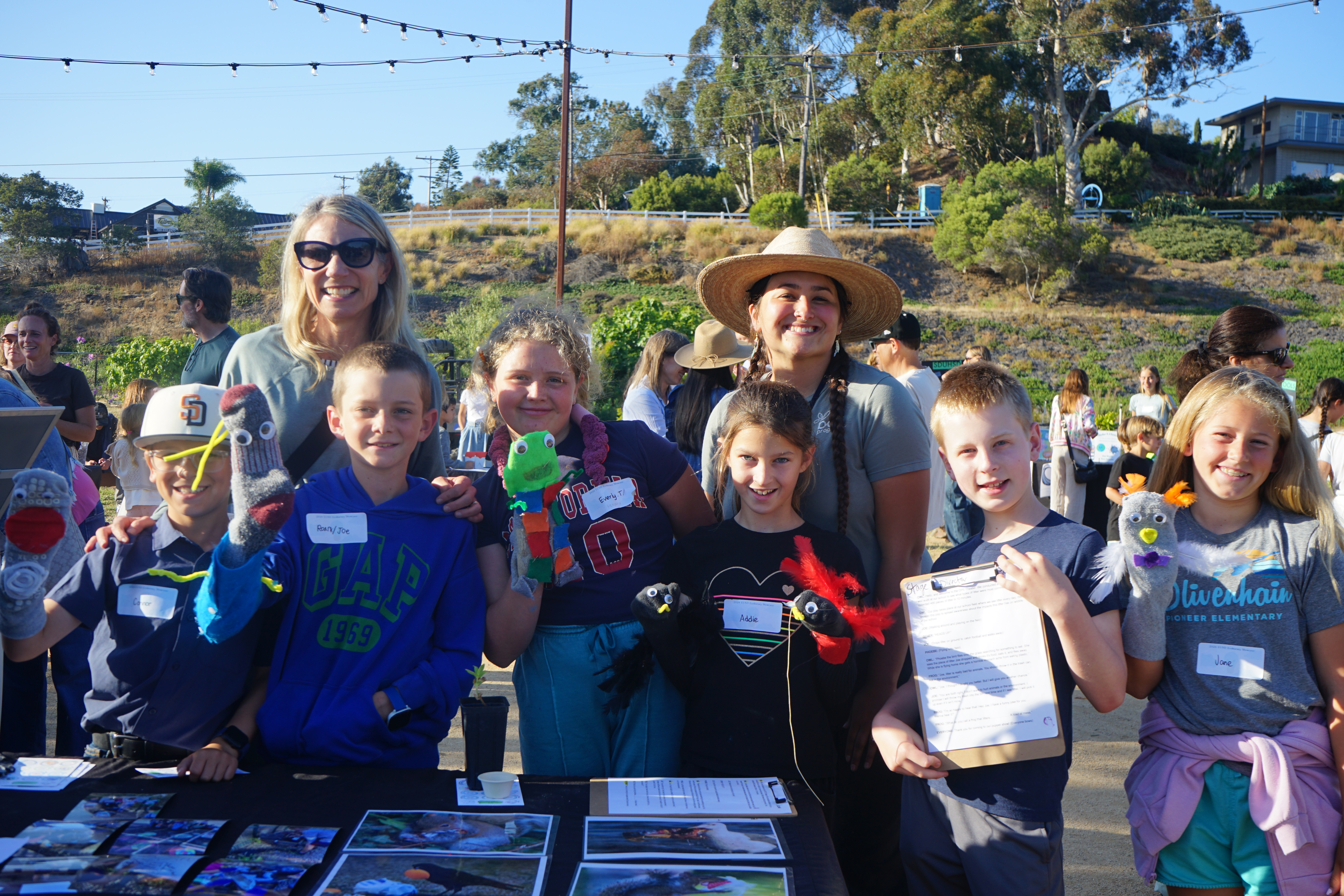 Six students stand with their teachers at their puppet show booth.