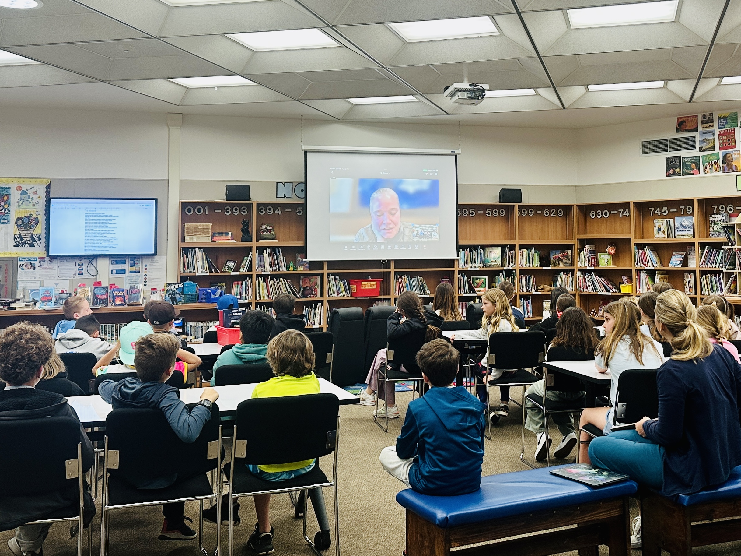 Upper-grade students watch a presentation from a field expert in the library.
