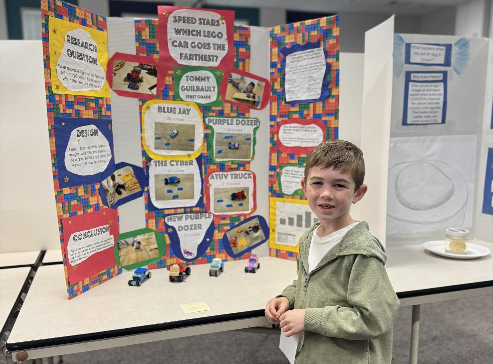 A student stands in front of his science fair project testing the speed of different lego cars they engineered.