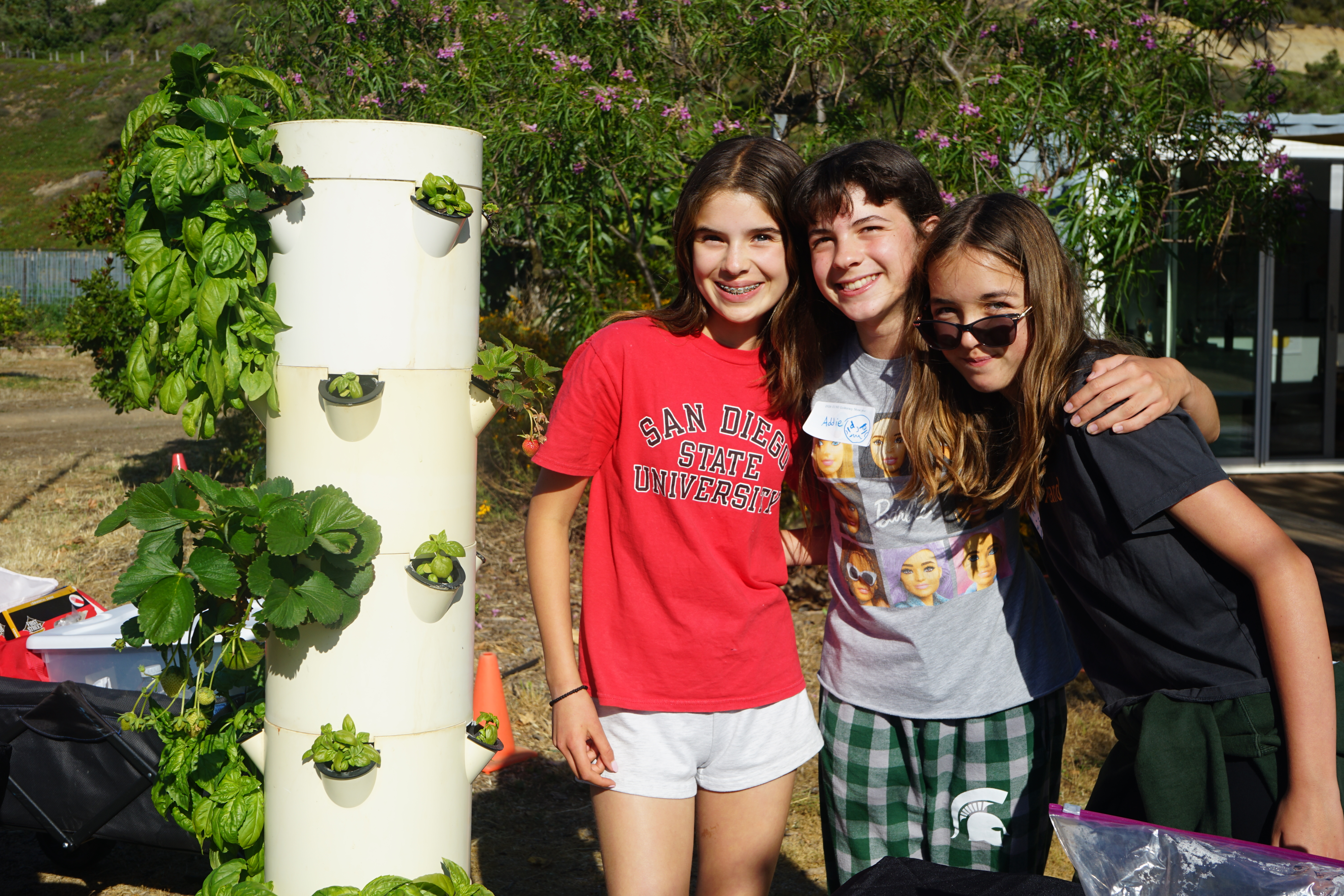 Three students stand next to the hydroponics station.