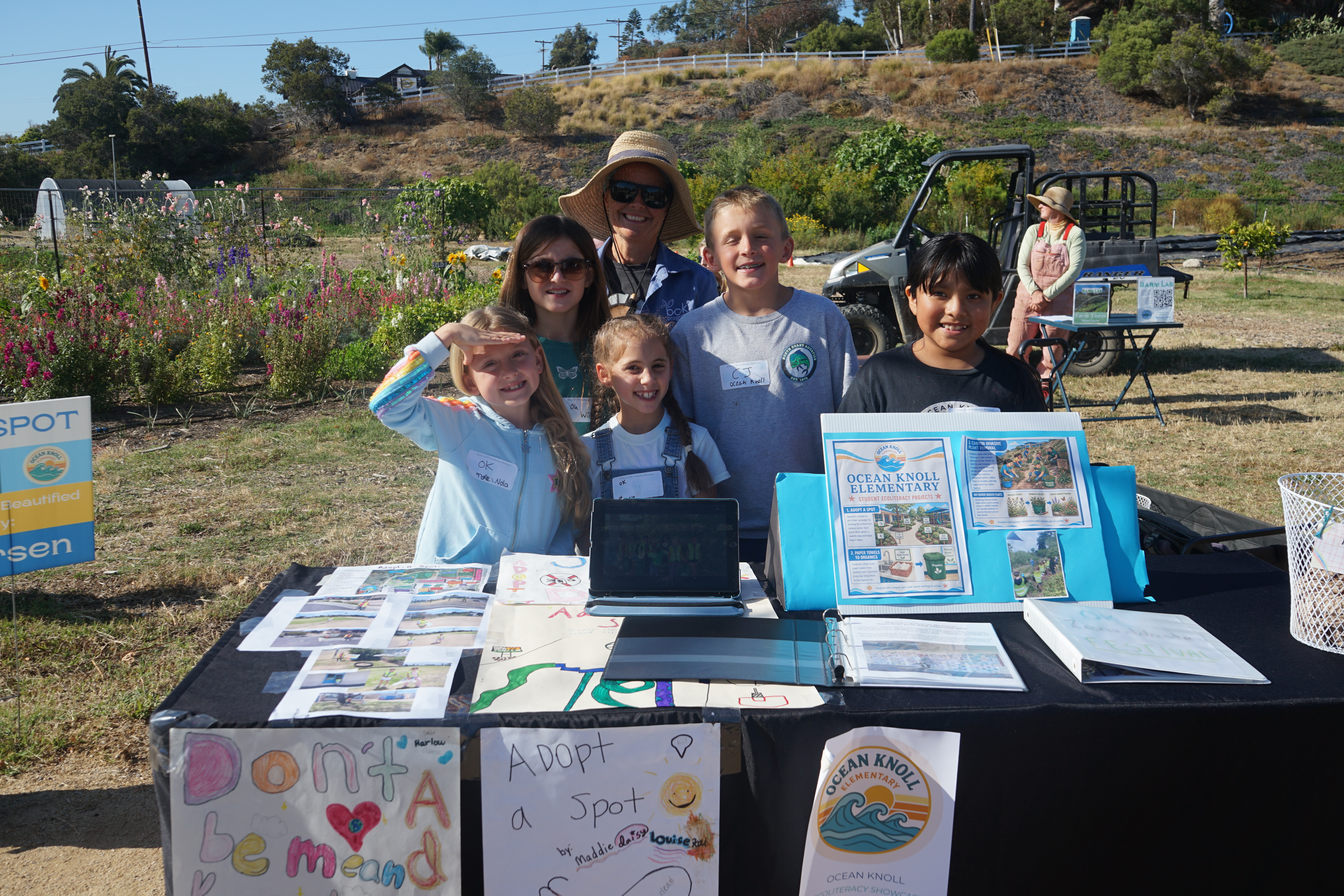 Five students and their teacher stand at their table talking about litter cleanup at their school.
