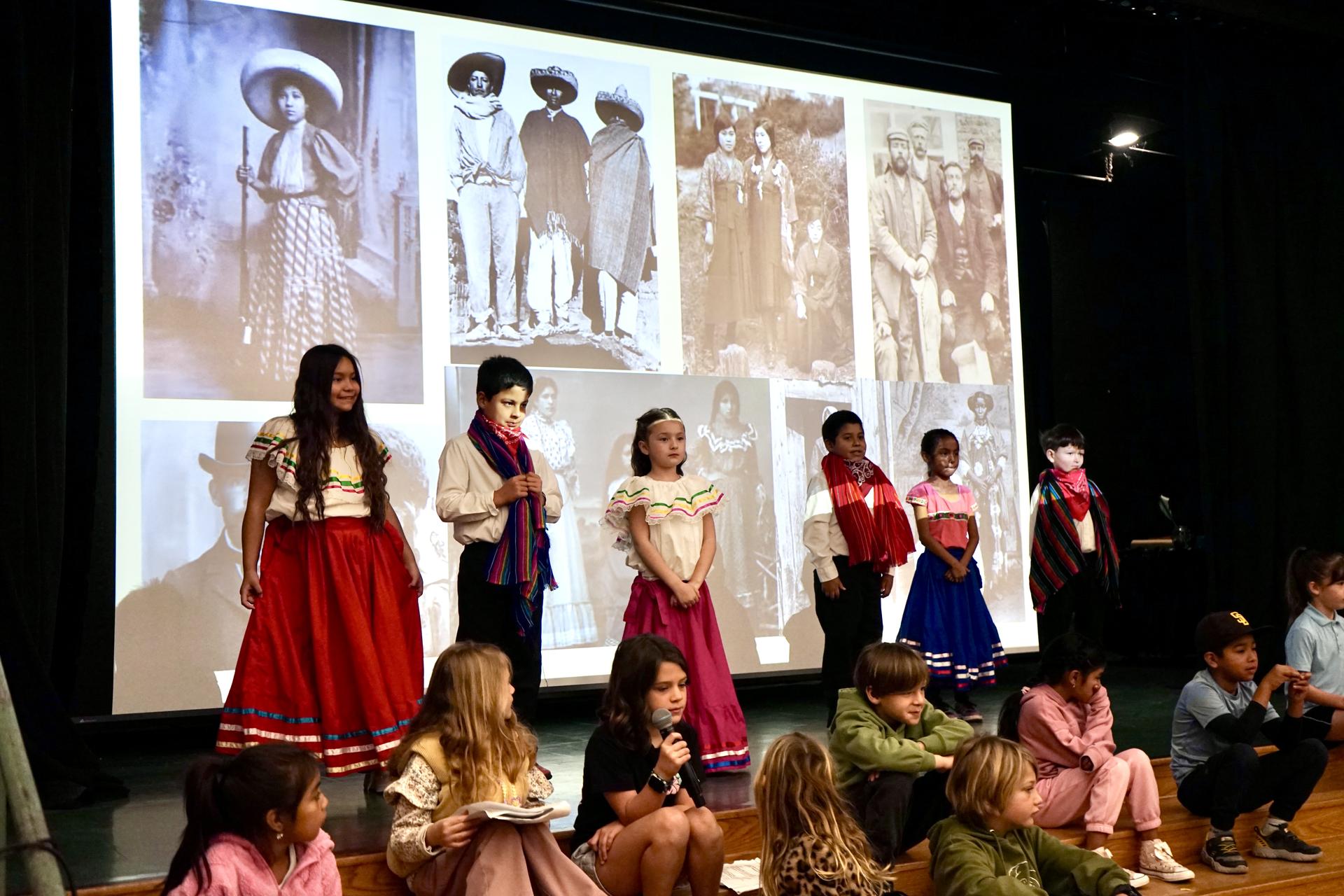 Six students stand on stage wearing traditional clothing from Mexico