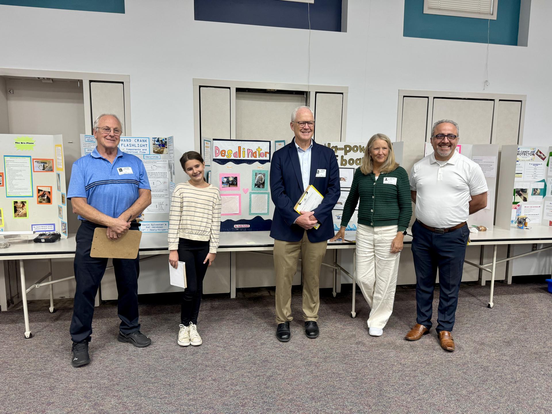 A student stands with three adults in front of science fair posters.
