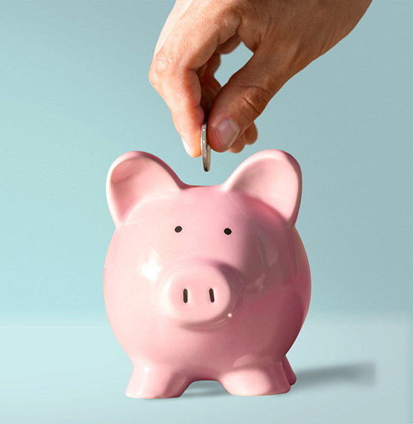 Hand putting money in a pink piggy bank.