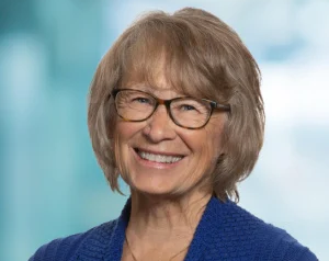 Professional headshot of Patty Wetterling. She wears a button with the number 11 on it in honor of her son.