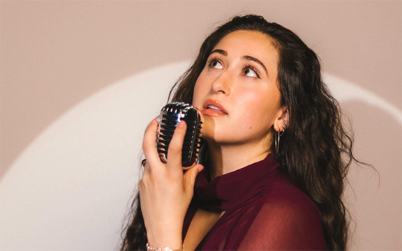 Musician Frankie Torres holds microphone as she looks up into the distance.