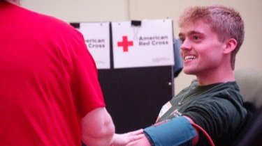 A man smiles and sits in a leaned-back chair as he gets is blood pressure measured by an American Red Cross nurse.