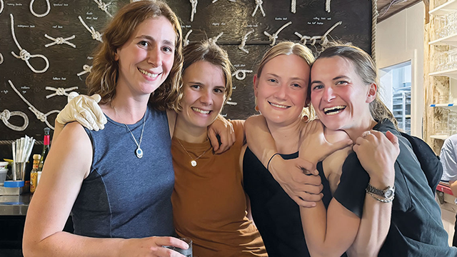 Four friends hug in front of a wall of knots.