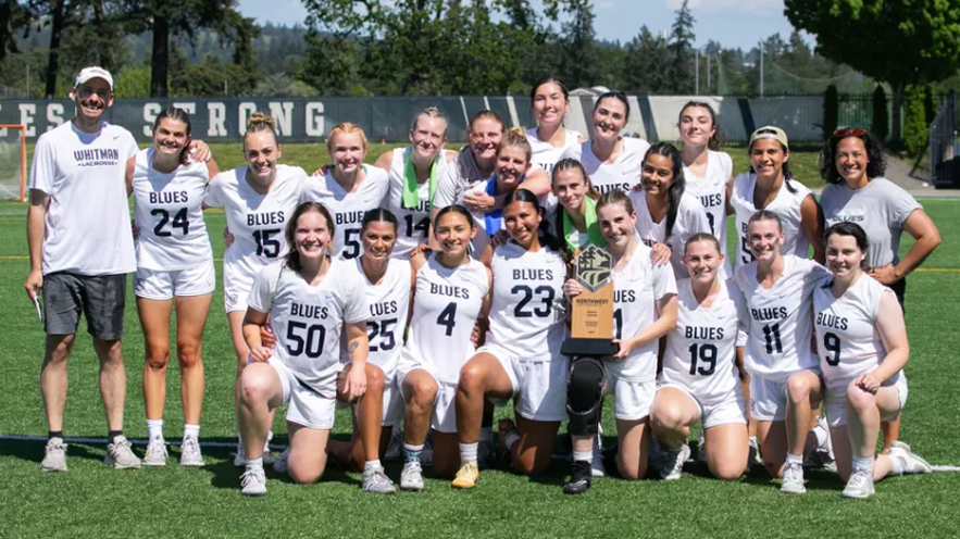 The Whitman women’s lacrosse team in white uniforms; one player holds a trophy