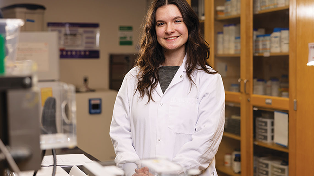 Sofia Del Fiol stands in a lab setting wearing a white lab coat