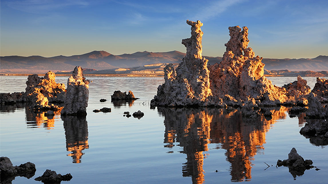 Jagged rock formations interrupt the stillness of Mono Lake with rolling hills visible in the distance