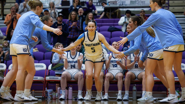 A Whitman Blues basketball player high fives a group of teammates on the court