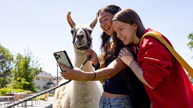 Two students take a selfie with a llama outside Cleveland Commons