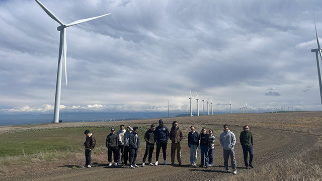 A group of students standing by several large wind turbines