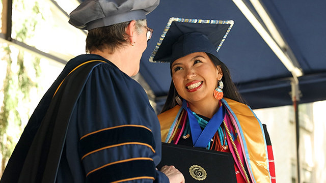 A student receives their diploma from President Bolton