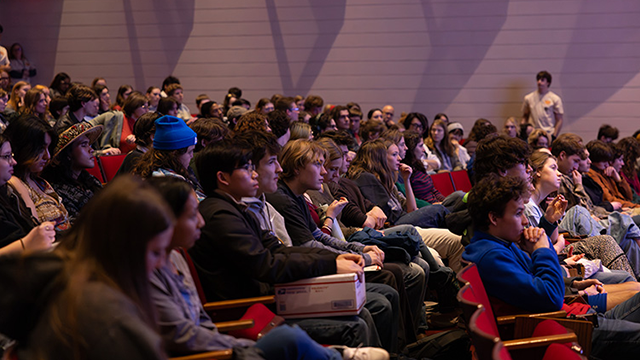 Several rows of seating are filled as audience members look towards an offscreen stage