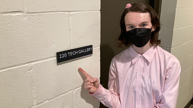 Artemis Gilbert points to a small sign installed next to a door that reads: “220 tech gallery