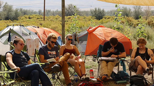 A group of people sitting outside in portable chairs with tents in the background