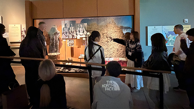 Iroha Konishi (arm extended) speaking to onlookers about a museum exhibit