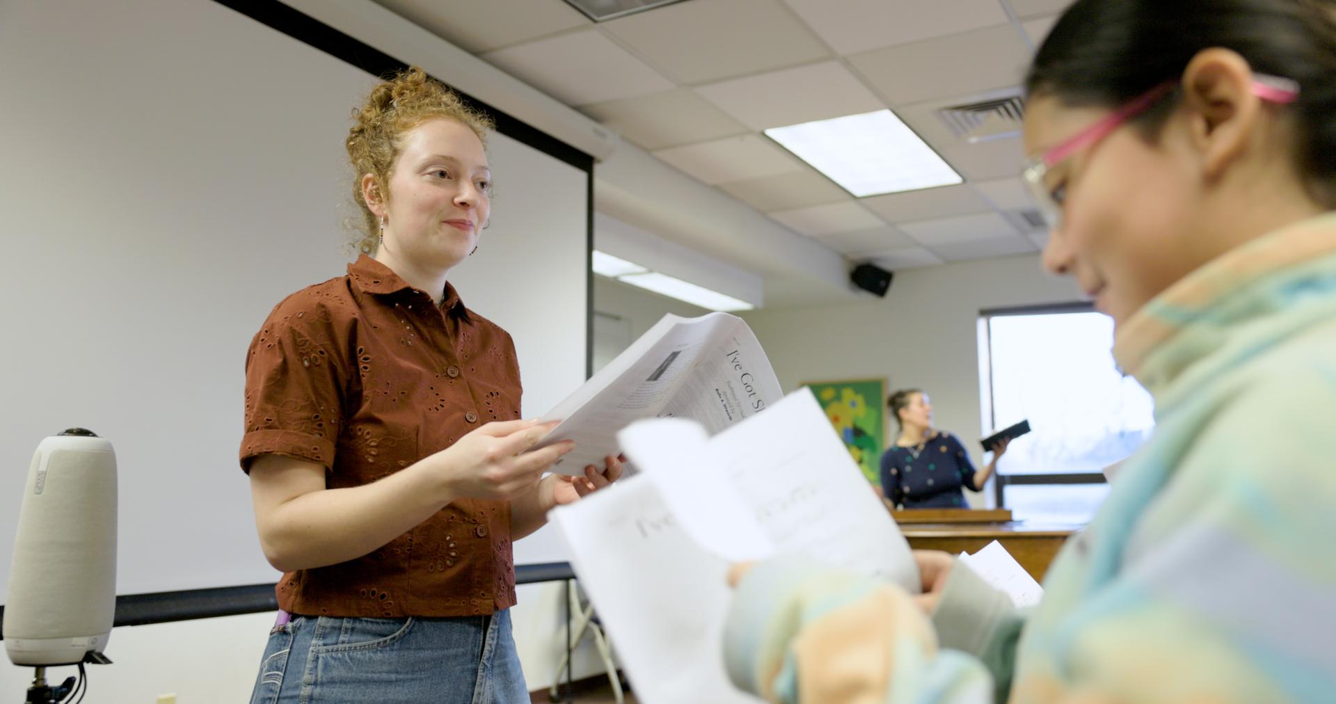 Millie Atack addresses a classroom of young students while holding sheet music