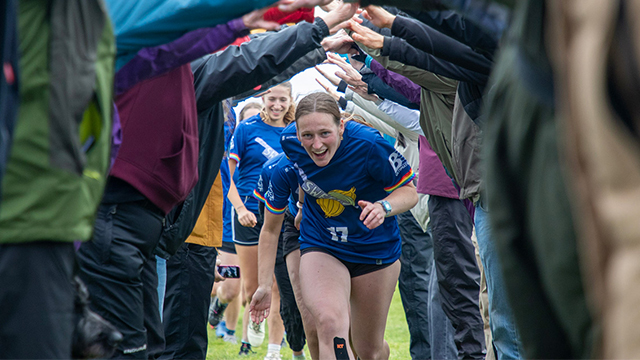 Ultimate players run between two rows of people holding their arms up to create a tunnel
