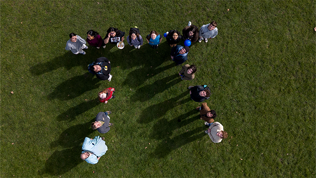 A drone shot of a group of people standing in the shape of the symbol for pi