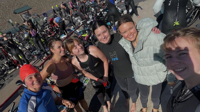 Six students take a selfie with lots of people and bicycles in the background