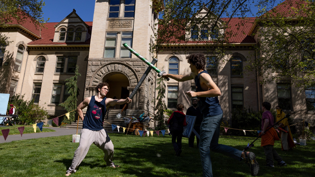 Two students mock fight with plastic swords in front of Memorial Building