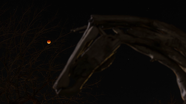 A red moon is visible on a black sky, with the blurred outlines of a horse head sculpture visible in the foreground