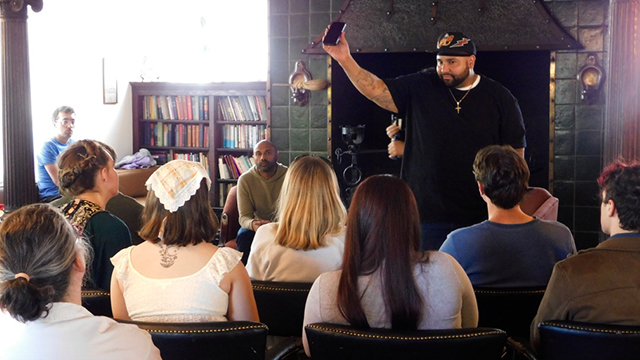 A presenter hold up a cell phone in front of a seated audience in Baker Center