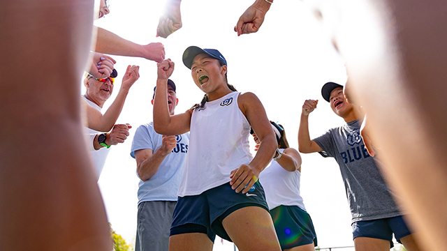 A tennis player celebrates a victory surrounded by their teammates and coaches