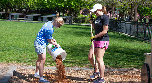 Natalie Lundberg empties a bucket of mulch, while Brenna Mack waits nearby with a rake