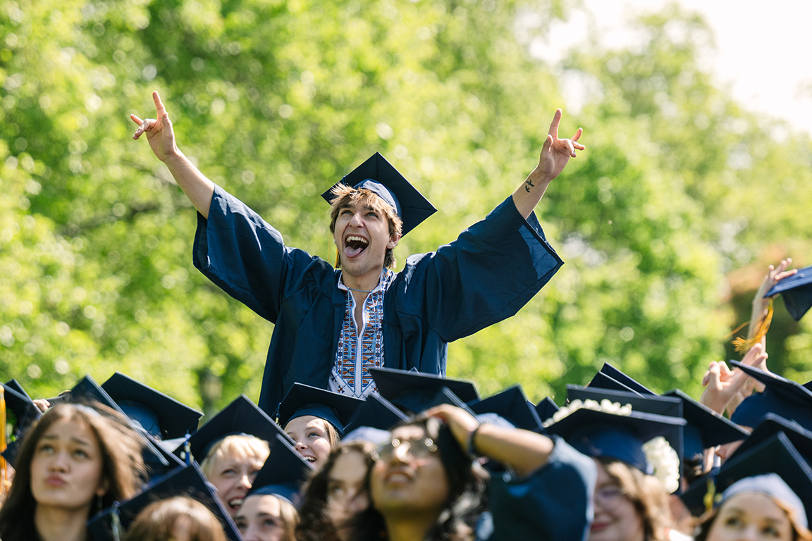 A student in graduation regalia raises both arms in celebration