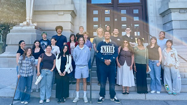 Five students stand in front of the trivia leaderboard pointing to a blue t-shirt held by the student in the center of the group