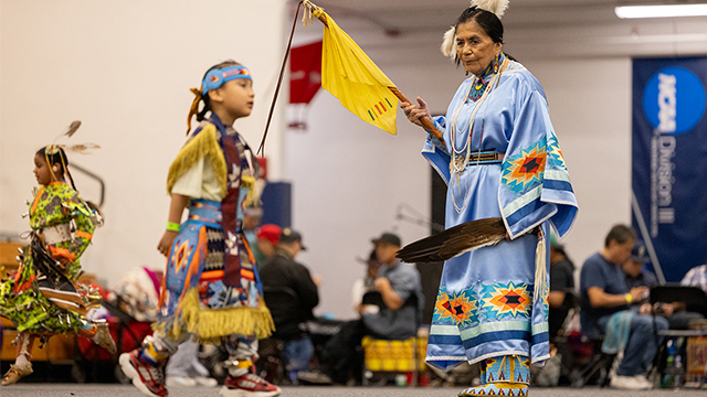 An older woman and two kids dancing in Native American regalia