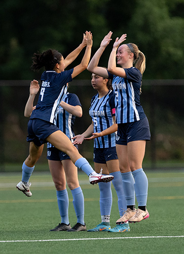 A group of soccer players in Whitman jerseys jump and high five each other 