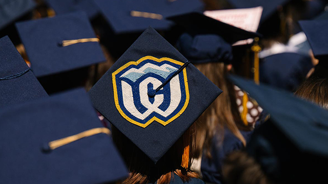 A graduation cap decorated with beads in the design of the Whitman athletics logo stands out in a crowd of other blue caps