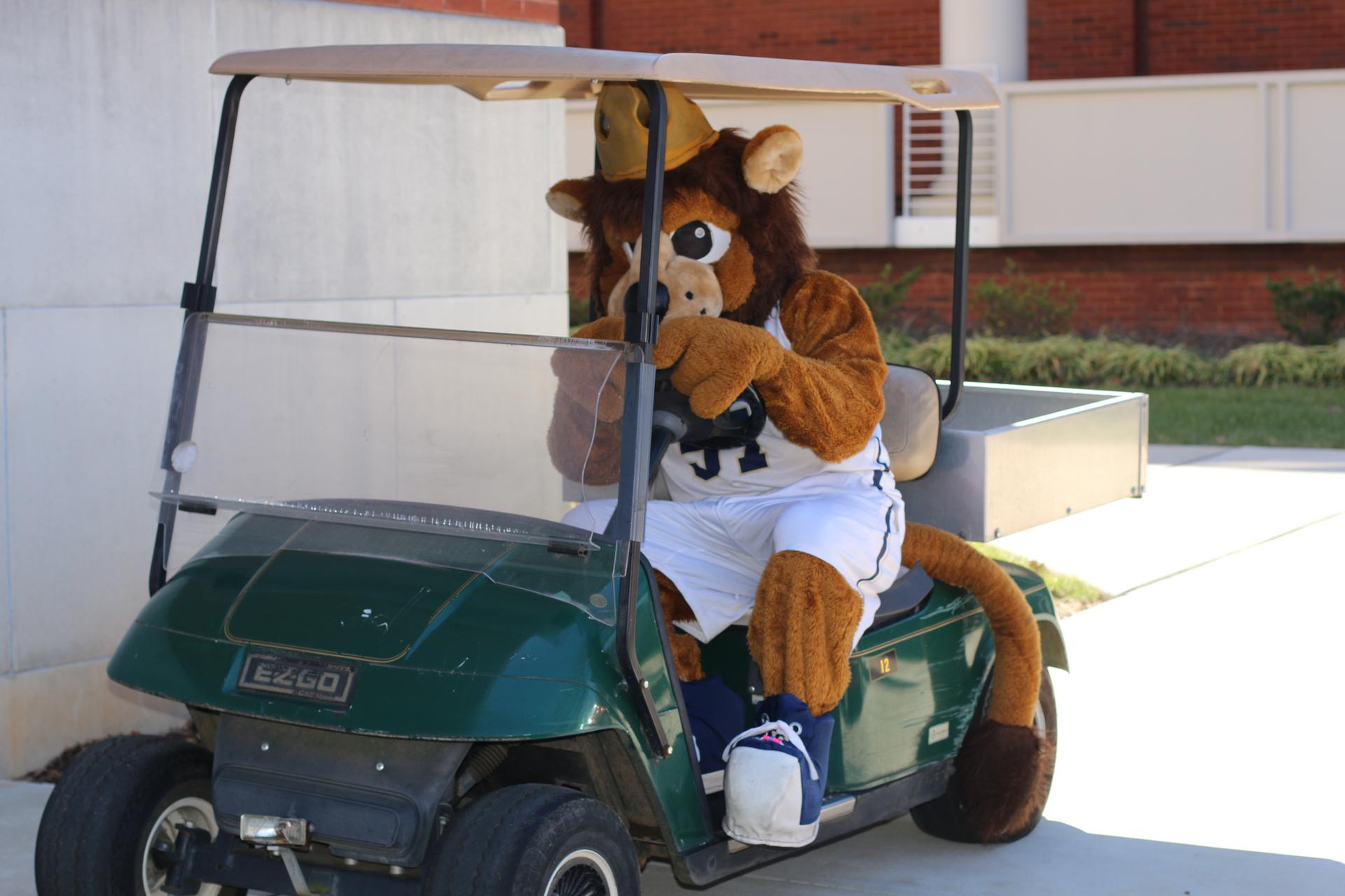 Rex the Mascot driving a golf cart through Queens University's campus