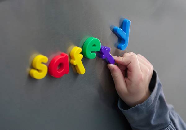 Close-up photo of a child's hand spelling the word safety with refrigerator magnets.
