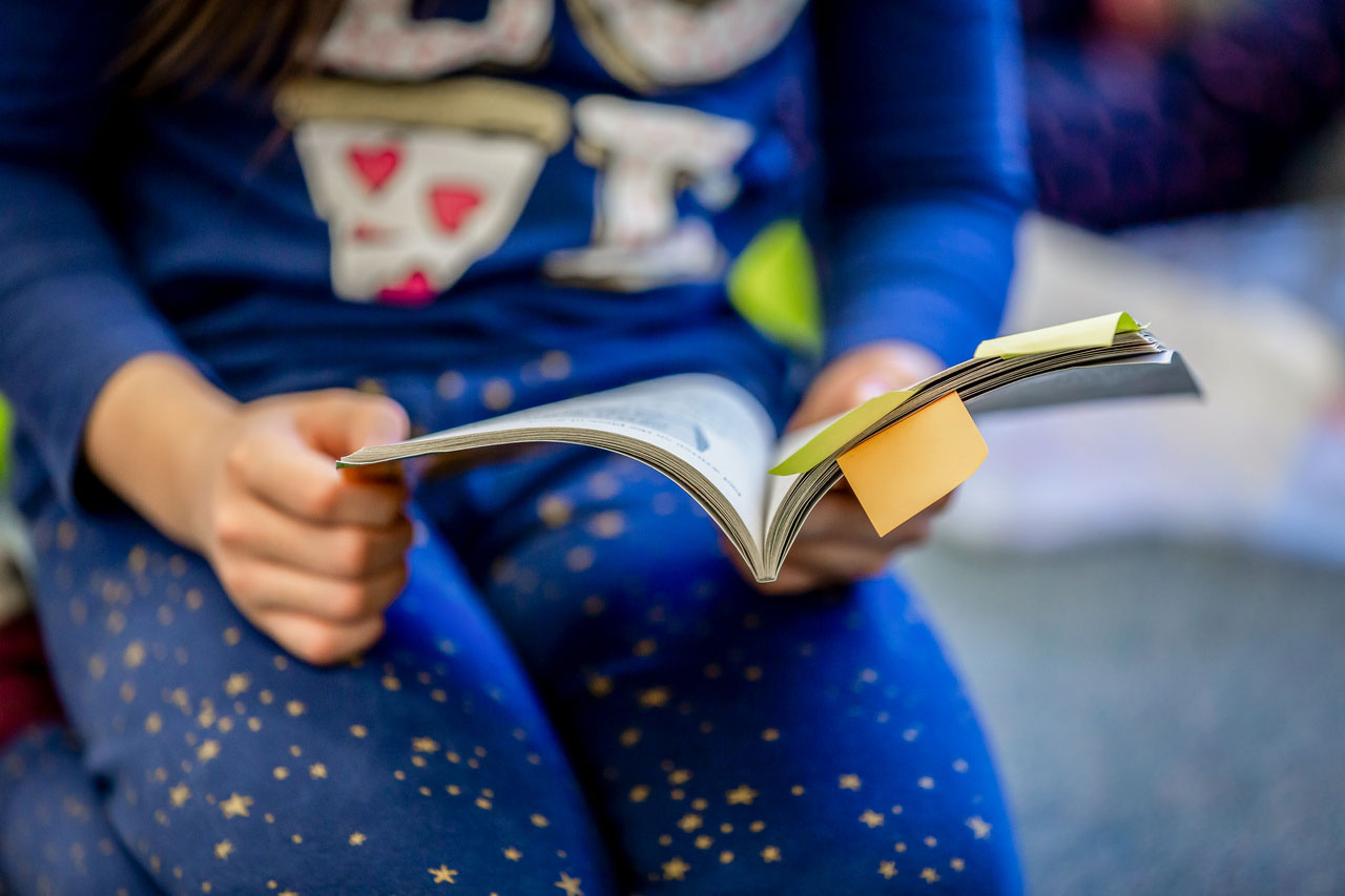 A third grader reads a book with some pages marked with sticky notes 