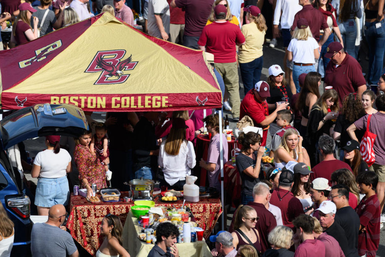 A Boston College tent at a football tailgate is surrounded by people