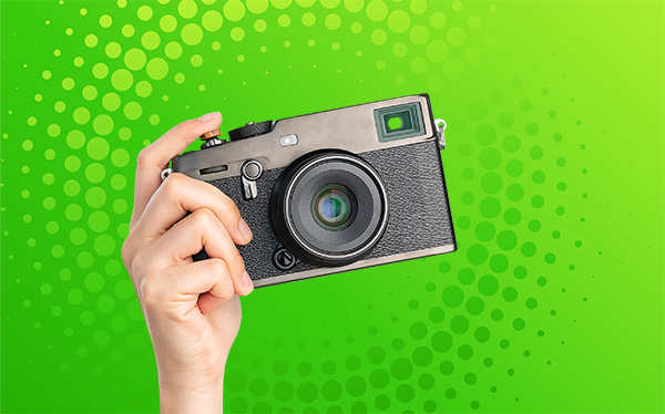 Hand holding a camera with green background.
