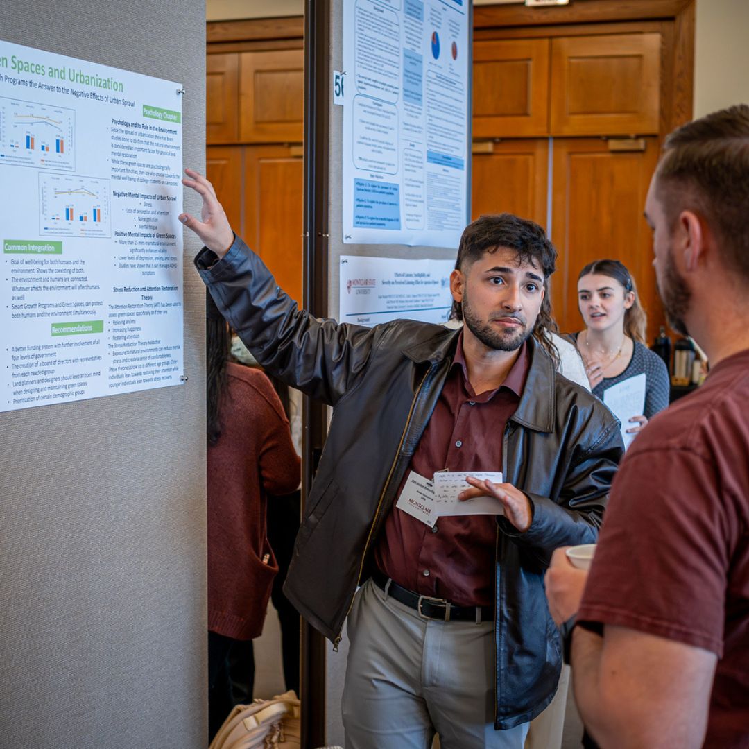 Student wearing business casual attire presenting his research at the 2025 Student Research Symposium.